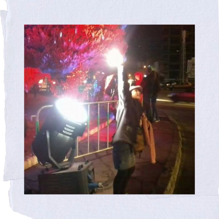 Foto de Aisha criança em Zahle, no Meinho do MUndo (Líbano) brincando com um canhão de luz. Sua mão está iluminada pelo feixe, e ela olha para frente com expressão de encantamento e curiosidade. Imagem carregada de memória, luz e simbolismo.