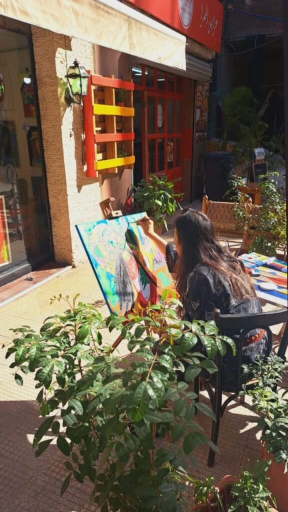 Artist Jeane Satie in her studio painting a colorful Godiva canvas, blending Brazilian soul and Beirut resilience.