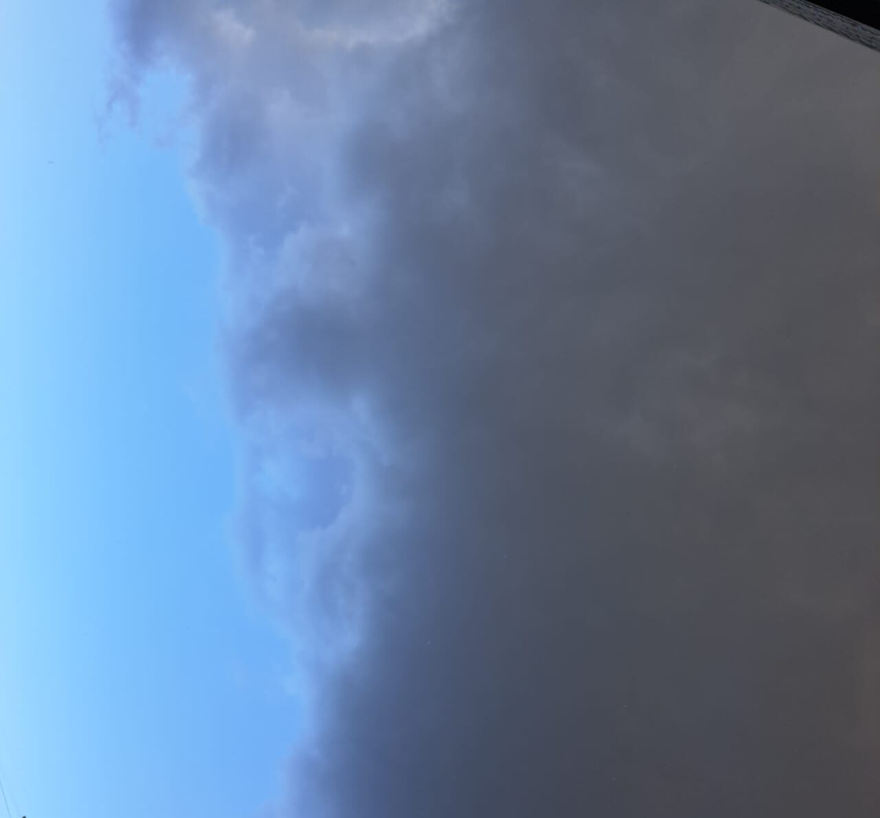 Fotografia capturada em Adma, Líbano, mostrando uma divisão nítida entre céu azul ensolarado e nuvens carregadas de chuva, separadas por uma linha quase imperceptível no horizonte. Imagem simbólica da desigualdade geográfica e emocional — usada como inspiração para o texto 'Na Fronteira da Chuva' por Jeane Satie.